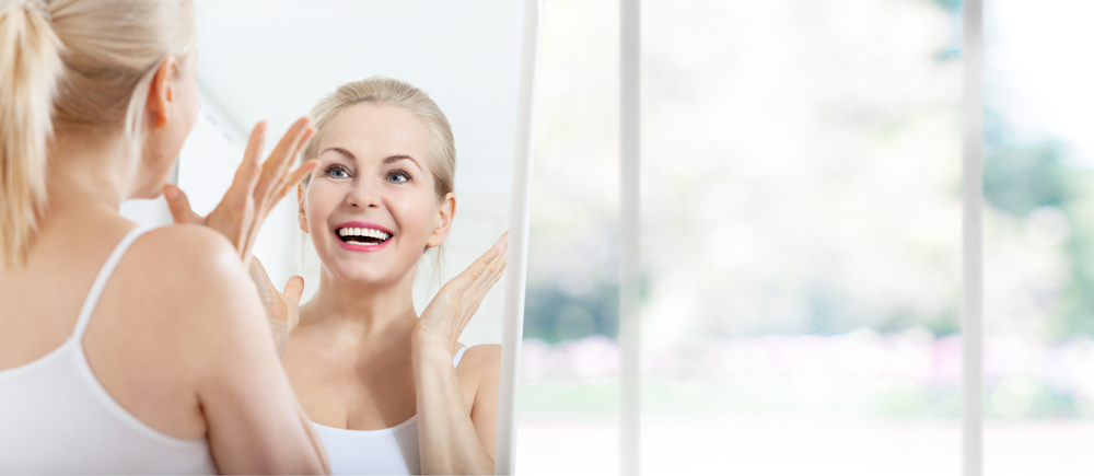 Woman smiles in the mirror, looking delighted with the results of her Morpheus8 skin rejuvenation treatment